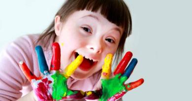 Menina com Síndrome de Down com tinta colorida nas mãos IStock/Getty Images